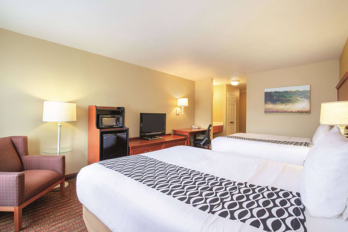 A hotel room with two beds, a desk with a computer, a TV, a chair, and a lamp.