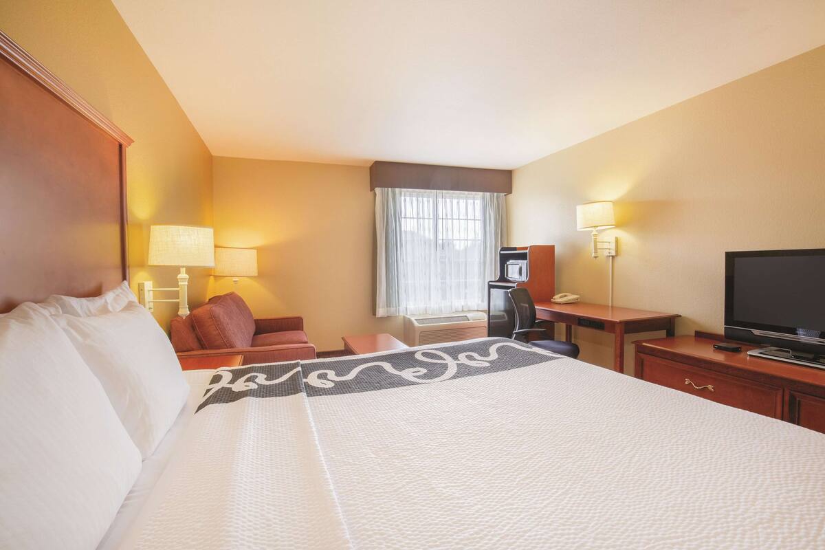 A hotel room with a large bed, a desk, a chair, a television, and a window with curtains.