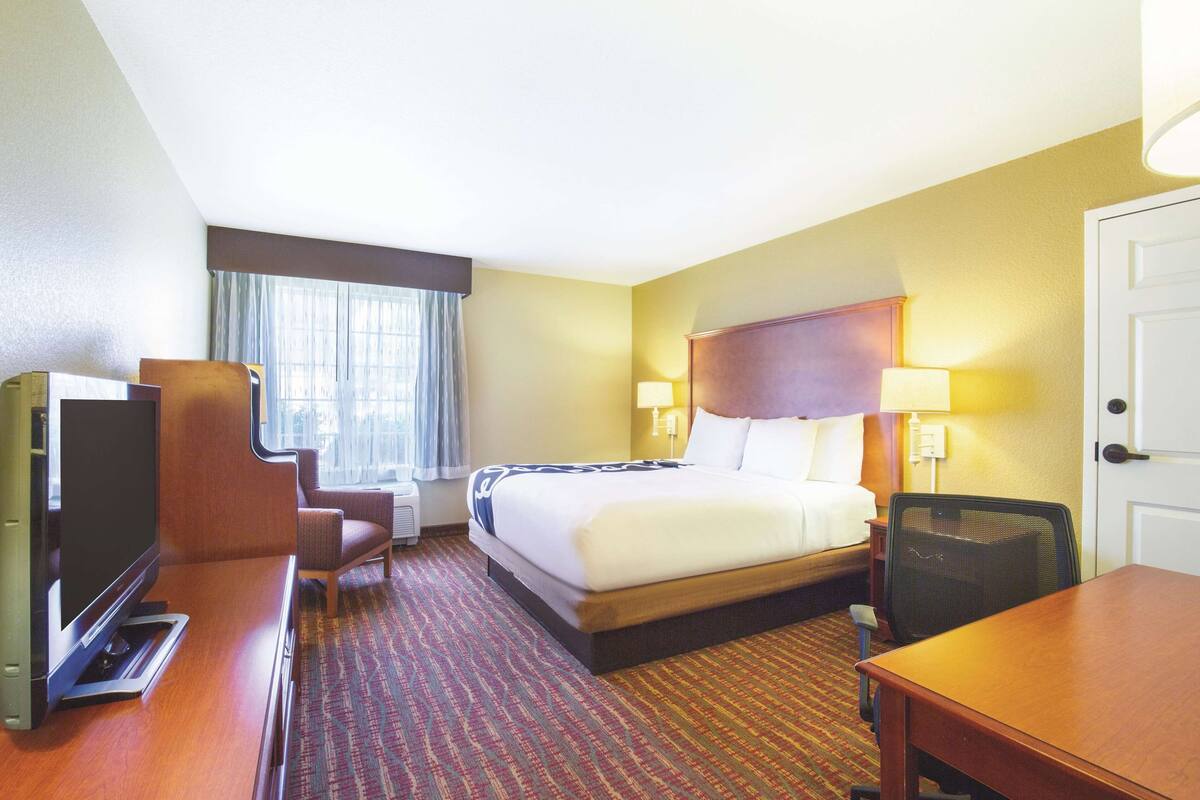 A hotel room with a bed, a desk, a TV, and a window with curtains.