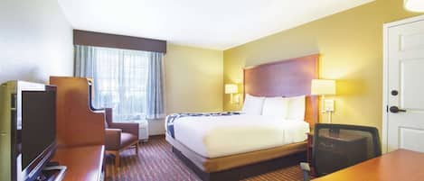 A hotel room with a bed, a desk, a TV, and a window with curtains.