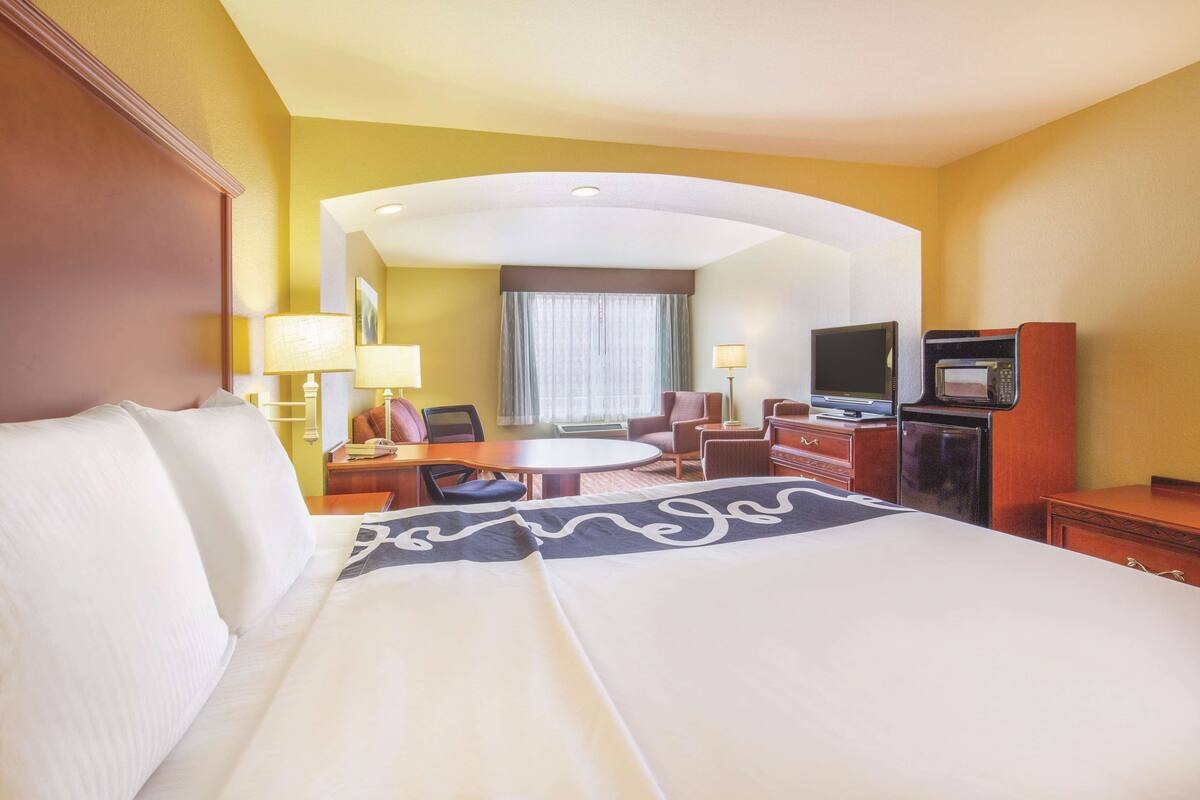 A hotel room with a large bed, a desk with a chair, a television, and a microwave.