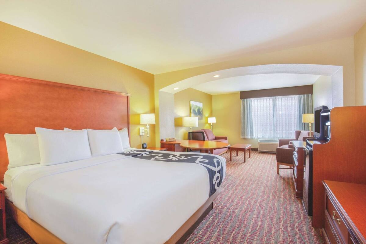 A hotel room with a large bed, a desk, a chair, a TV, and a window with curtains.