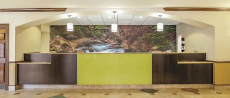 Un área de recepción con mostrador verde, un mural de cascada y piso de baldosas.