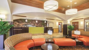 A lobby with a curved orange sofa, a reception desk, and a wall mural of a waterfall. - La Quinta Inn & Suites by Wyndham Bentonville (Bentonville)