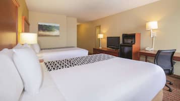 A hotel room with two beds, a desk, a TV, and a chair.