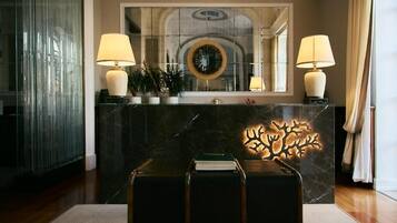 A lobby with a marble reception desk, two lamps, a mirror, and a decorative tree sculpture.