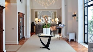A spacious hallway with a modern chandelier, a reception desk, and a seating area with a small table and chairs. - Palazzo del Corso (Gallipoli)
