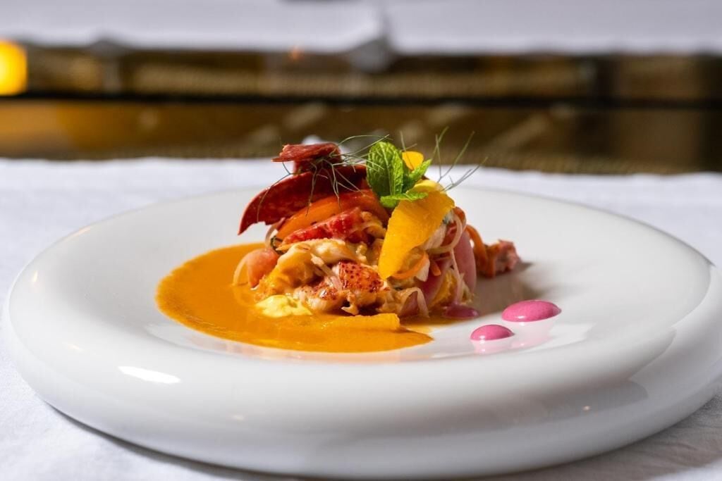 A white plate with a seafood dish, garnished with herbs and pink spheres.