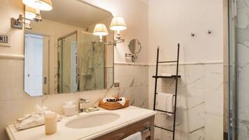 A bathroom with a large mirror, two wall-mounted lamps, a sink, a towel rack, and a shower area.