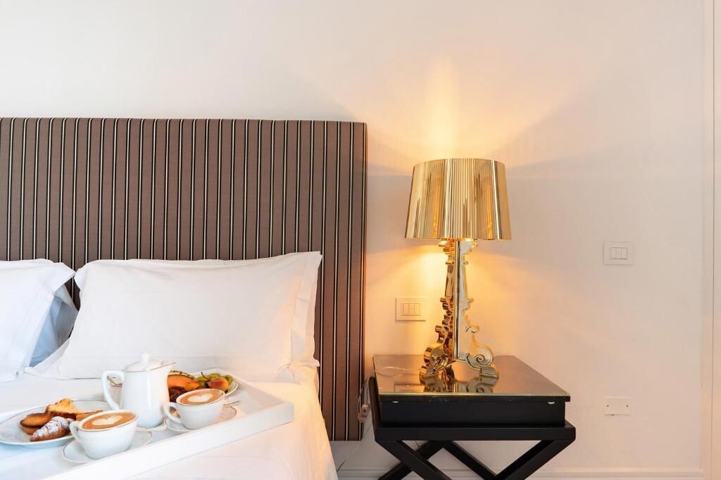 A hotel room with a bed, a tray with breakfast, a bedside table with a lamp, and a wall with a vertical panel.