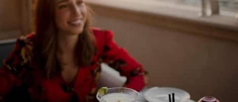 Iemand zit aan een tafel met een drankje en een glas water, met uitzicht op de zee.