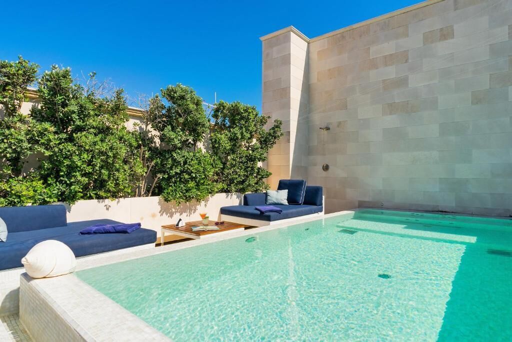 An outdoor swimming pool with a blue sofa and a small table with a drink.