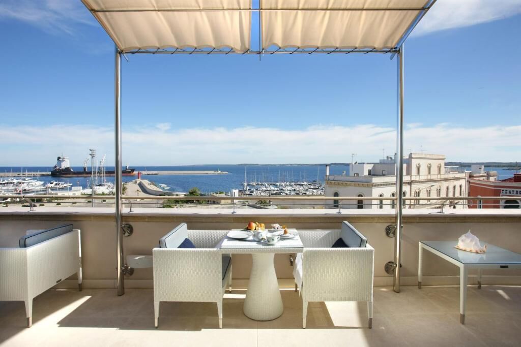 A terrace with a table and chairs, overlooking a marina and buildings.
