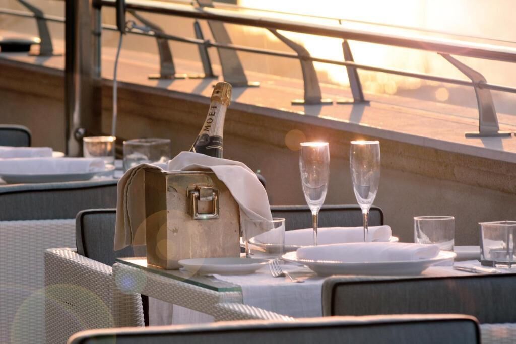 Een eettafel gedekt met champagne, twee glazen en borden, met uitzicht op een zonsondergang.