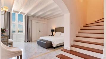 Un dormitorio con cama, mesita de noche, lámpara, ventana con cortinas, una escalera y vista al cielo.