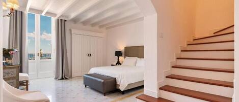 A bedroom with a bed, a nightstand, a lamp, a window with curtains, a staircase, and a view of the sky.