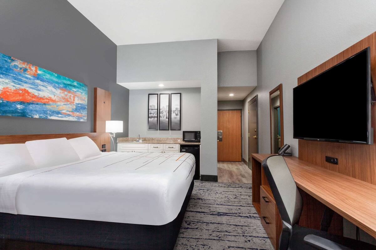 Ein Hotelzimmer mit einem großen Bett, einem Schreibtisch, einem Flachbildfernseher, einer Mikrowelle und einer kleinen Küchenzeile.