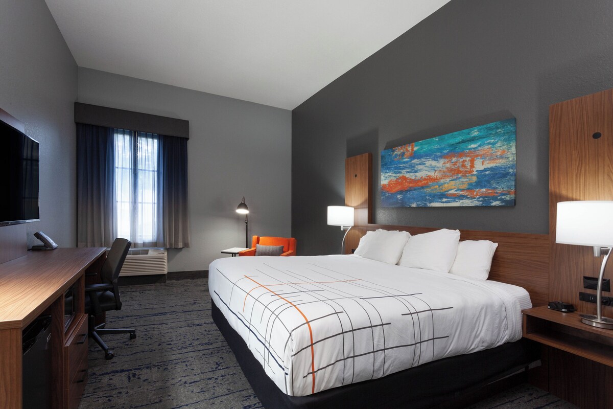 A hotel room with a large bed, a desk, a chair, a TV, and a painting on the wall.