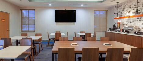 A conference room with a large table, chairs, a flat-screen TV, and a kitchenette area.