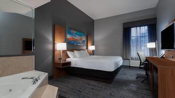 A hotel room with a large bed, two bedside lamps, a desk with a chair, a TV, and a bathroom with a bathtub and sink.