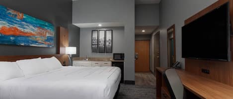 A hotel room with a large bed, a desk, a television, and a painting on the wall.