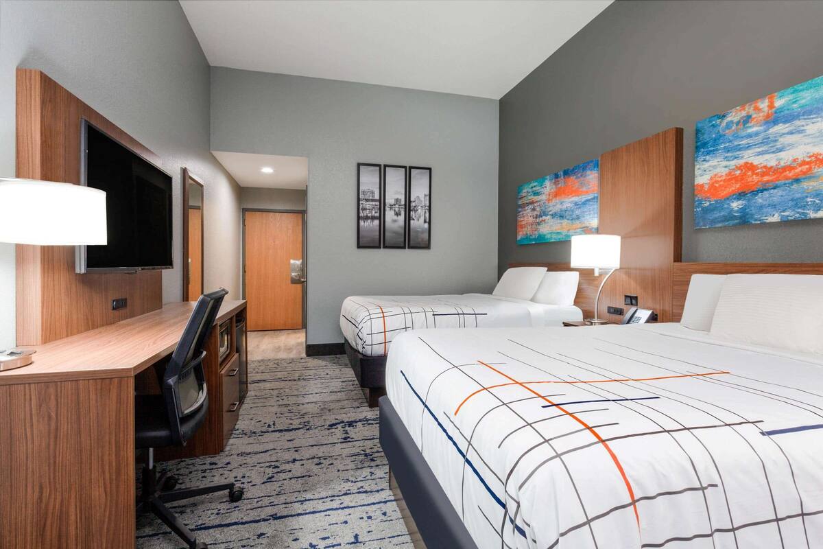 Ein Hotelzimmer mit Schreibtisch, zwei Betten, einem Fernseher und Bildern an der Wand.