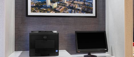 A desk with a printer and monitor, a framed cityscape picture above, and a patterned wall.