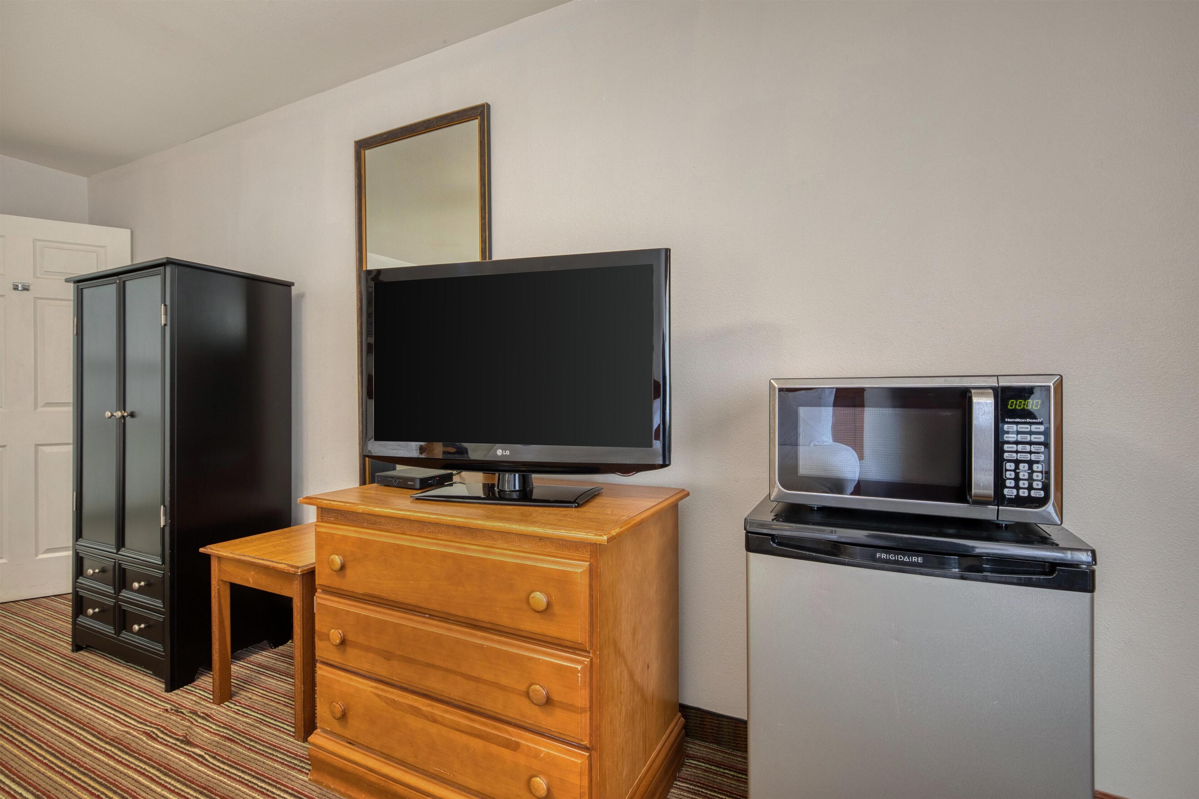 Une chambre d’hôtel avec une commode en bois, un téléviseur à écran plat, un four à micro-ondes et une armoire noire.