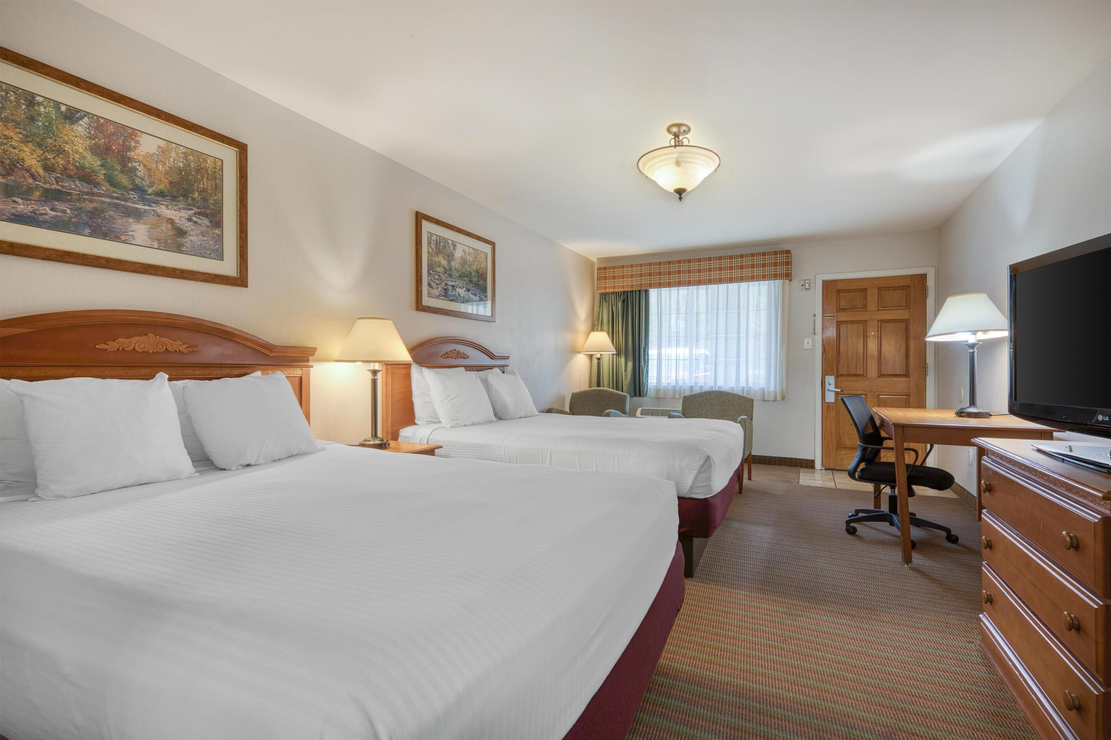 A hotel room with two beds, a desk, a television, and a window with curtains.