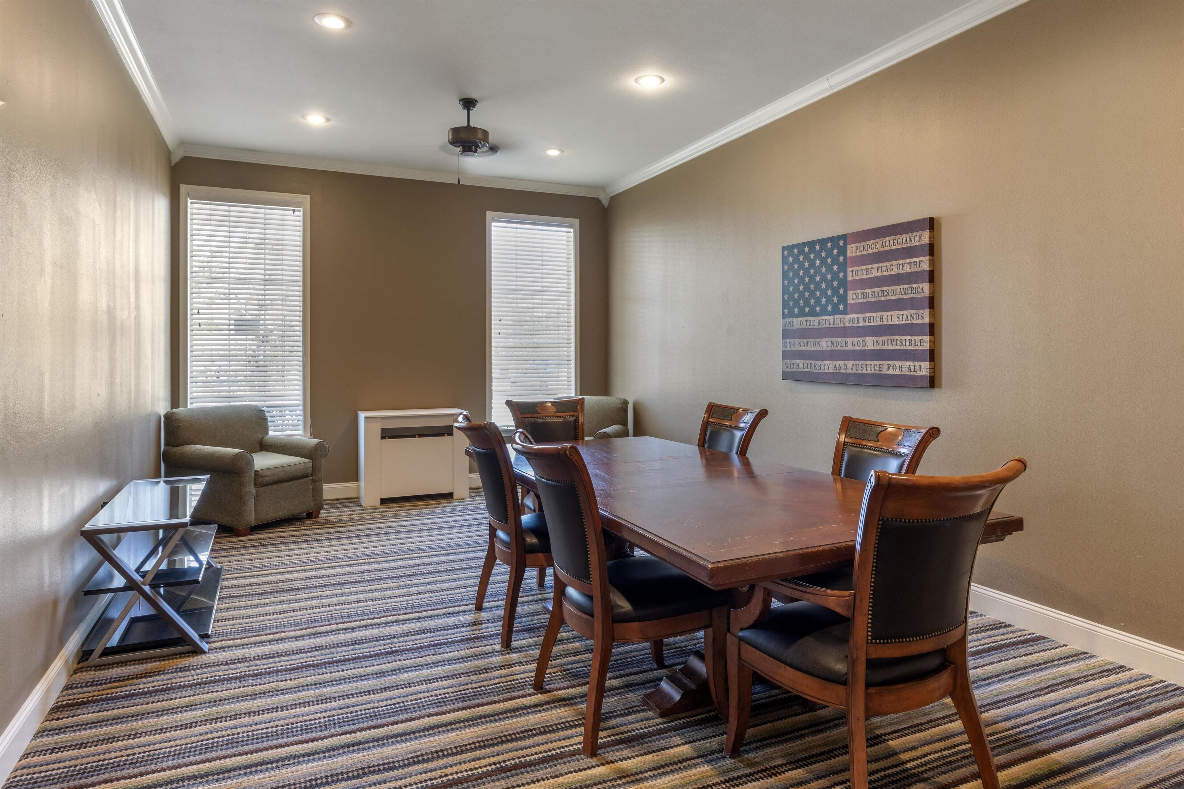 A conference room with a large wooden table, six chairs, and a flag on the wall.
