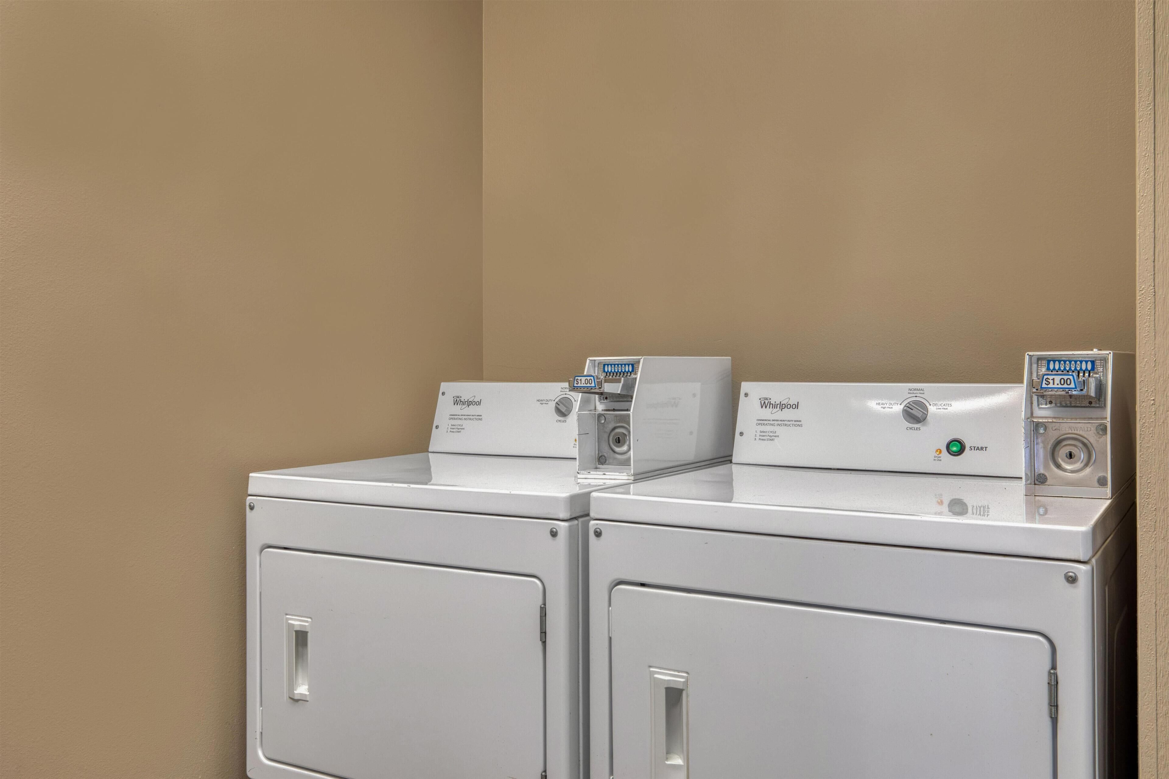 Two front-loading Whirlpool washers in a corner with beige walls.