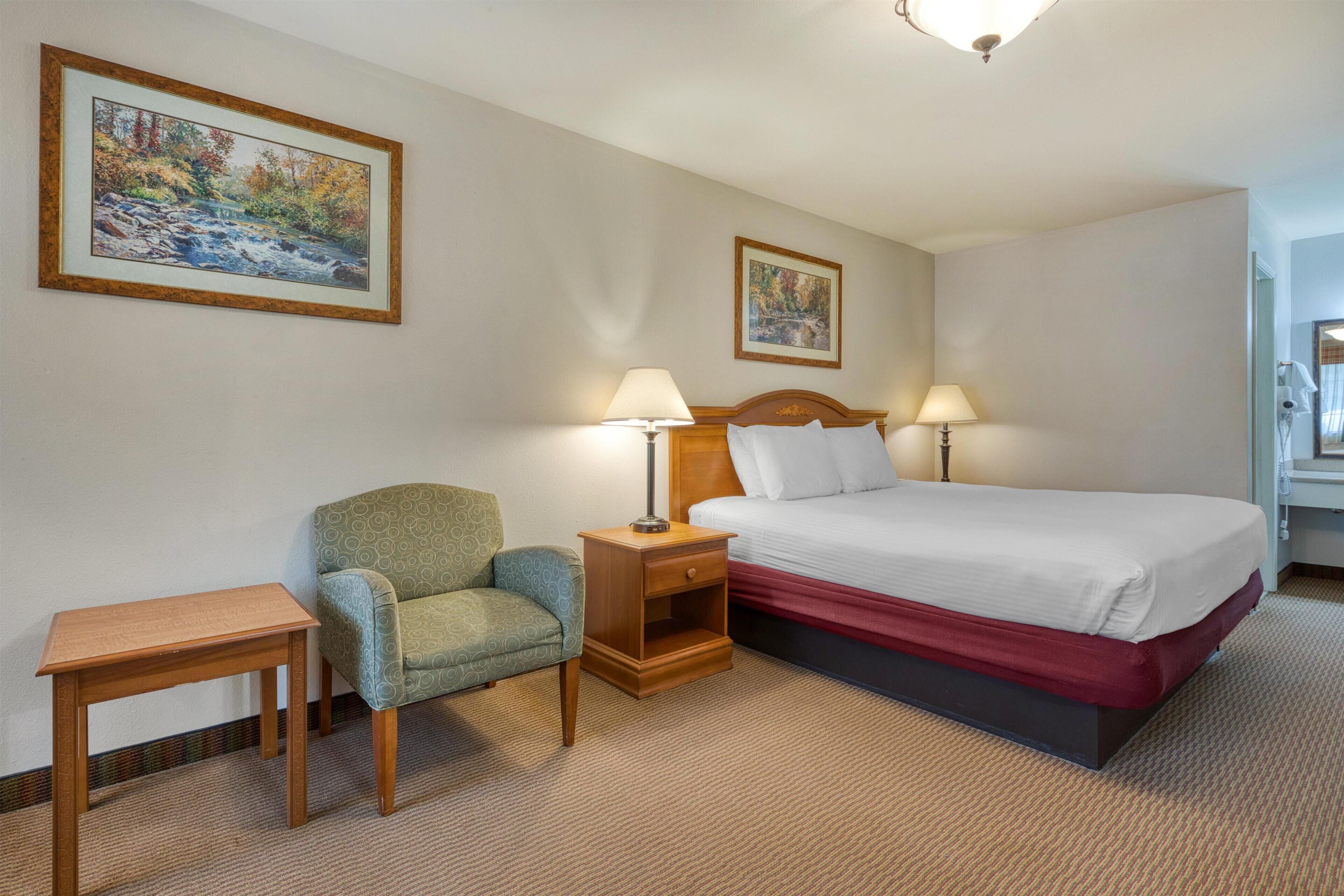Habitación de hotel con cama, dos mesitas de noche, una silla y dos lámparas fijadas a la pared.