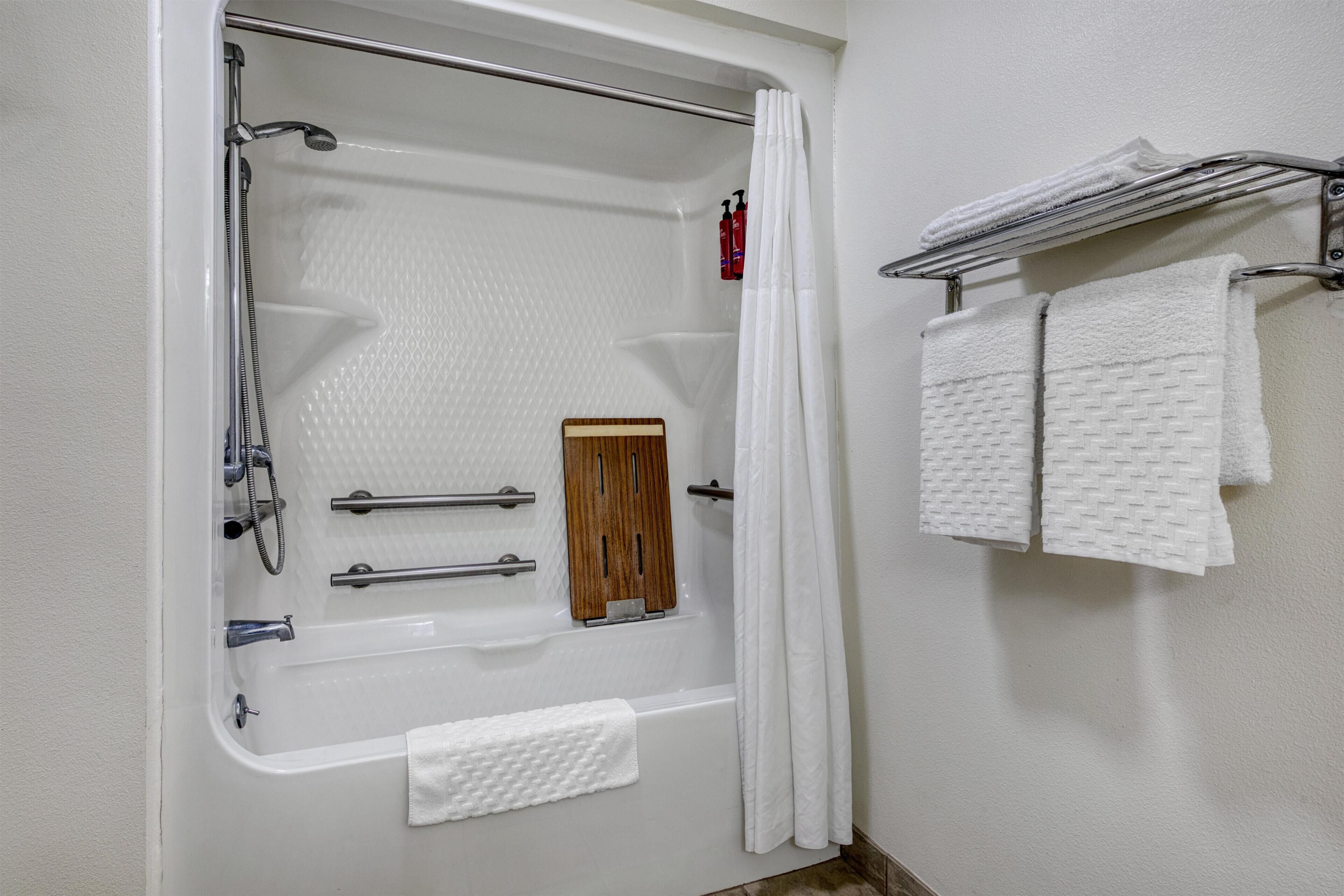 A bathroom with a bathtub, shower, and a towel rack with multiple towels.