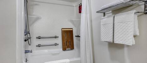 Un baño con bañera, ducha y un perchero con varias toallas.