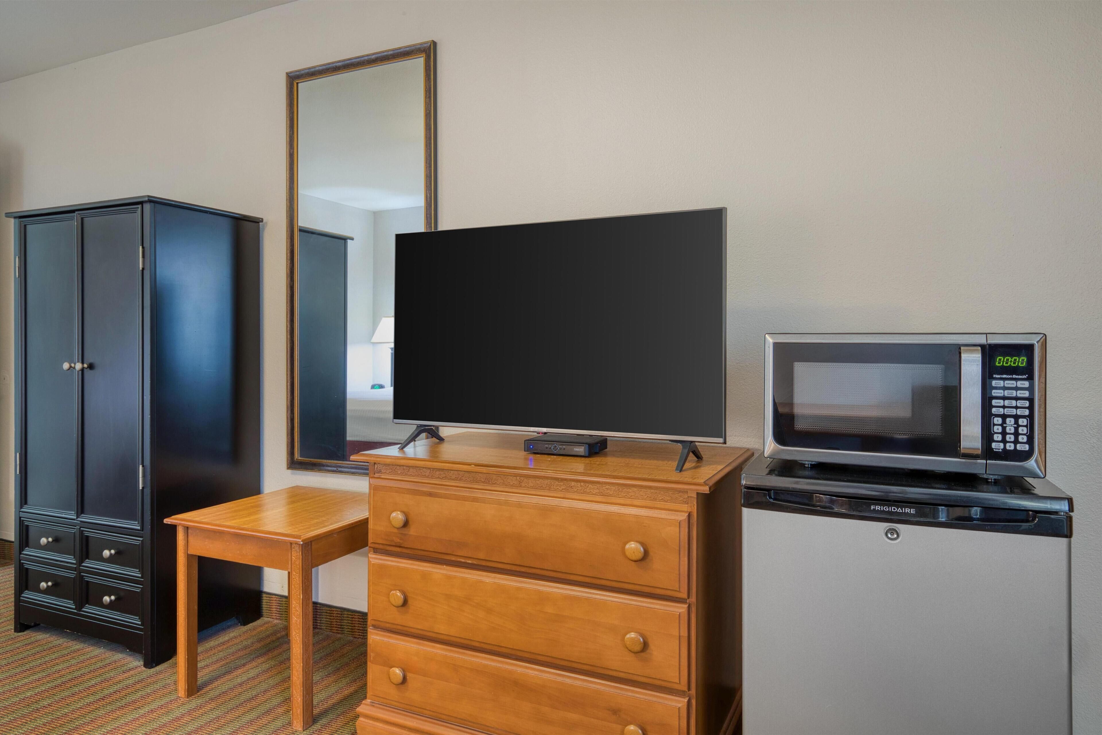 A hotel room with a wooden dresser, a flat-screen TV, a microwave, and a wardrobe.