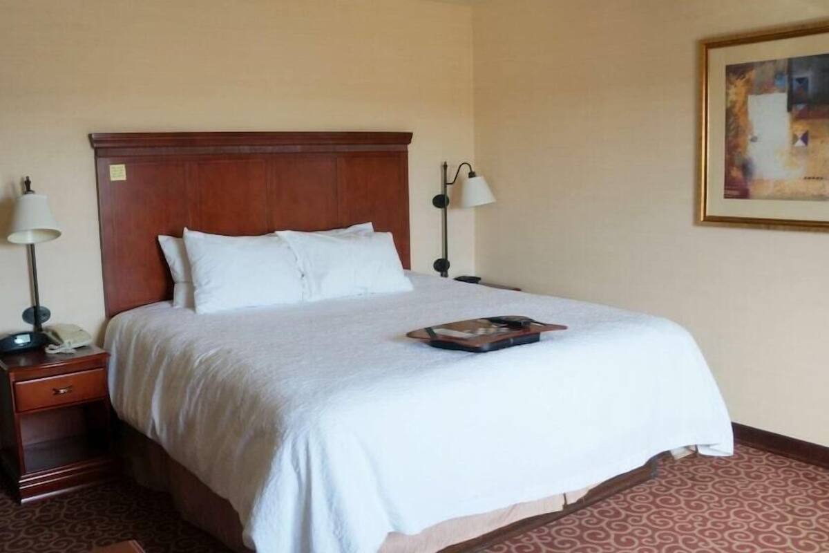 A hotel room with a large bed, two bedside tables, a nightstand, a lamp, and a painting on the wall.