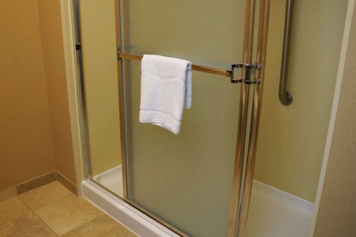 A glass-enclosed shower with a white towel hanging on a metal bar.