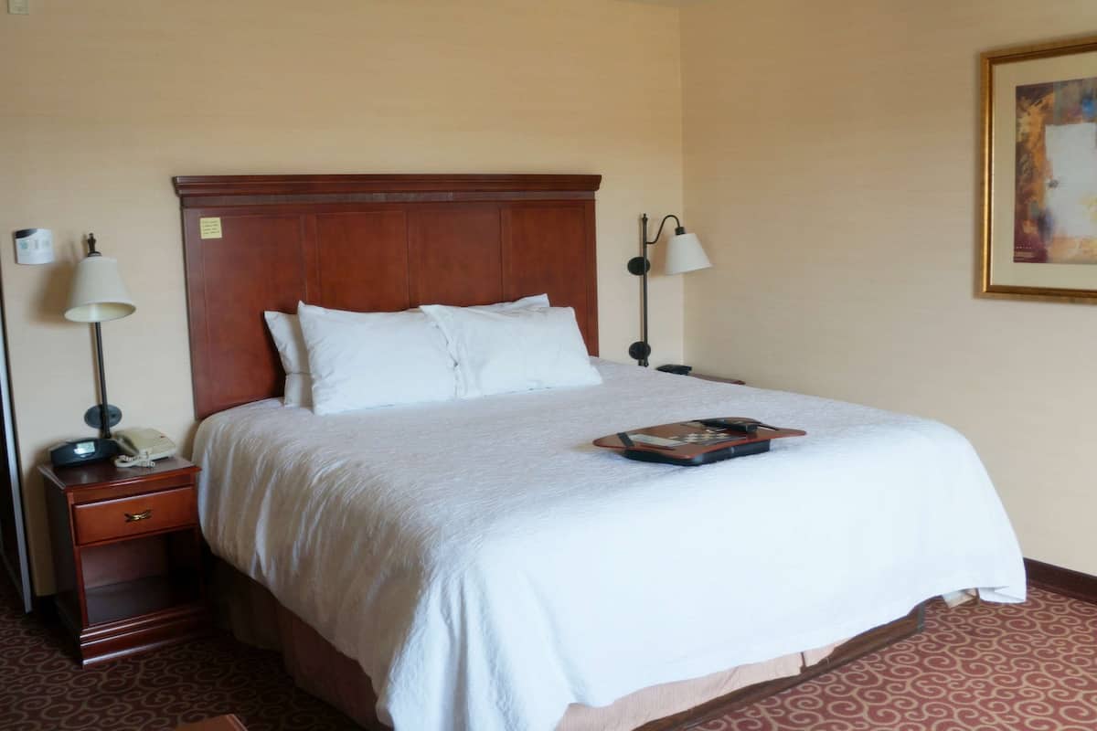 A neatly made bed with white linens, a wooden headboard, and two bedside lamps.