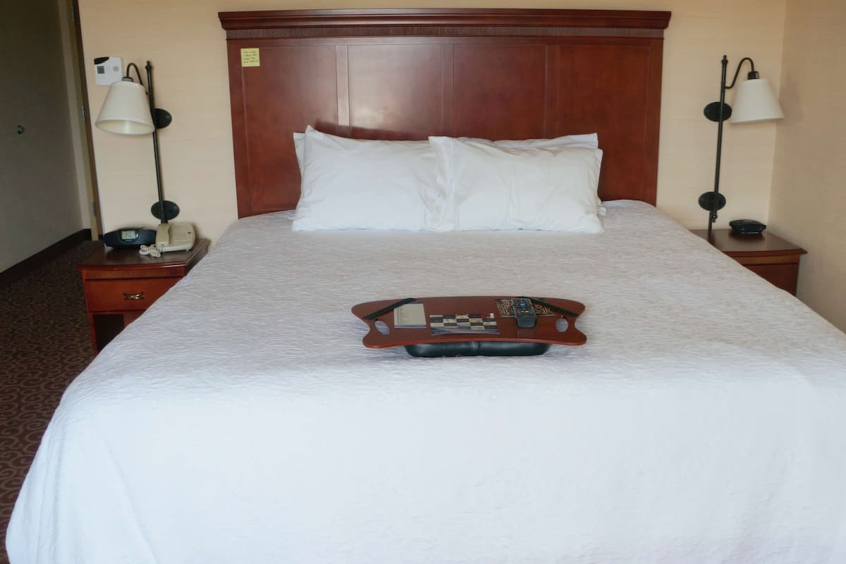 A hotel room with a large bed, two nightstands, a wooden headboard, and a tray table with a chessboard and remote control.