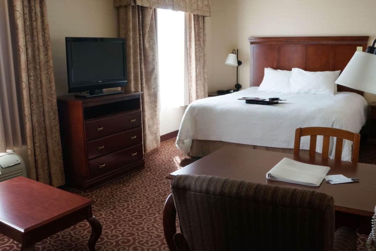 A hotel room with a bed, a desk with a chair, a television on a dresser, a telephone, and a lamp.