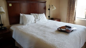 A neatly made bed with white linens, a wooden headboard, a bedside table with a lamp, and a small tray with a remote control.