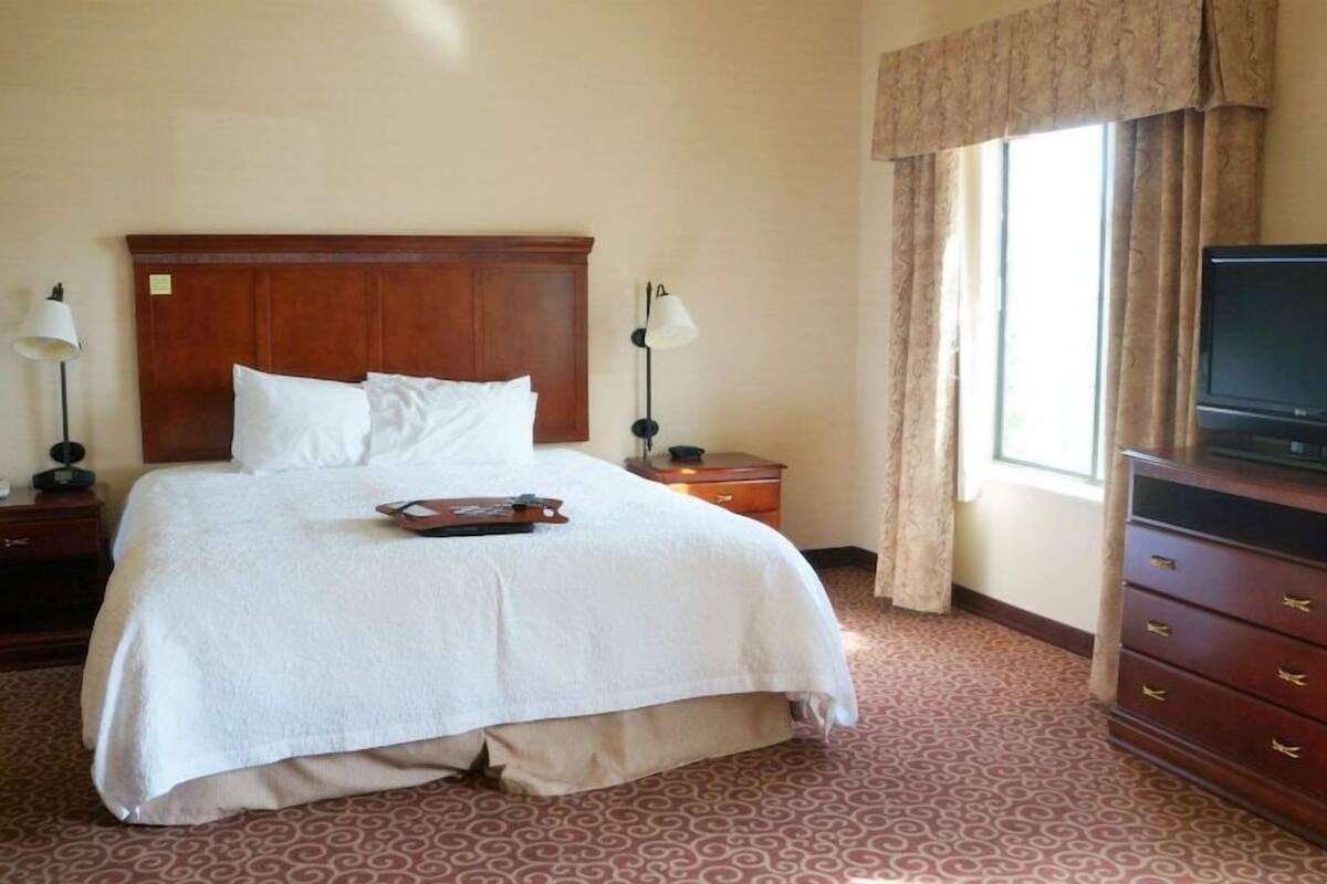 A hotel room with a large bed, a television on a dresser, and a window with curtains.