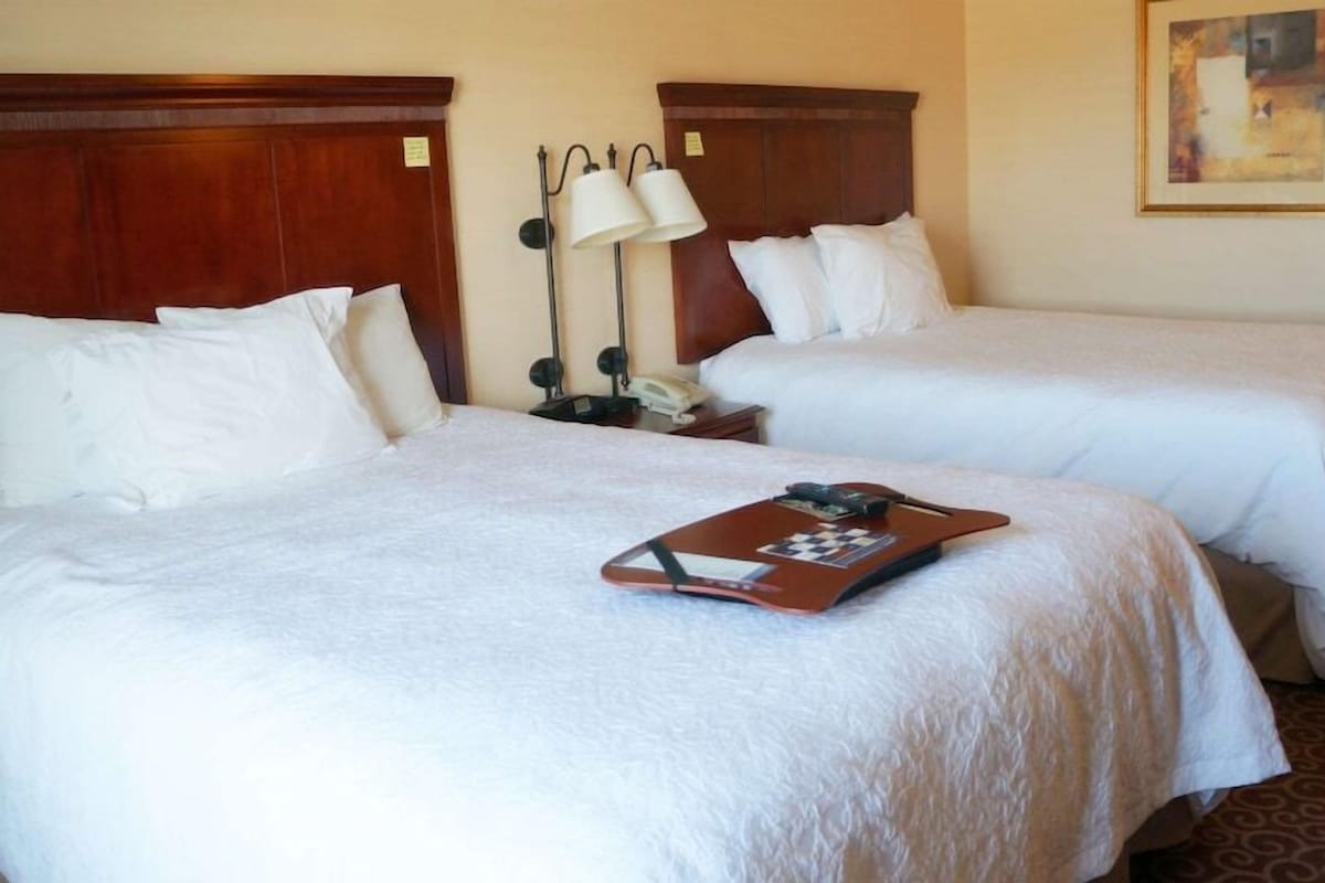 Two beds with white linens, a tray with items, and a lamp between them.