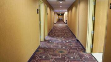 A hotel hallway with patterned carpet, yellow walls, and doors on both sides.