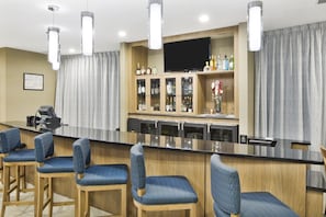 A bar area with a long counter, multiple bar stools, and a cabinet with liquor bottles. - Holiday Inn Augusta West I-20 by IHG (Grovetown)