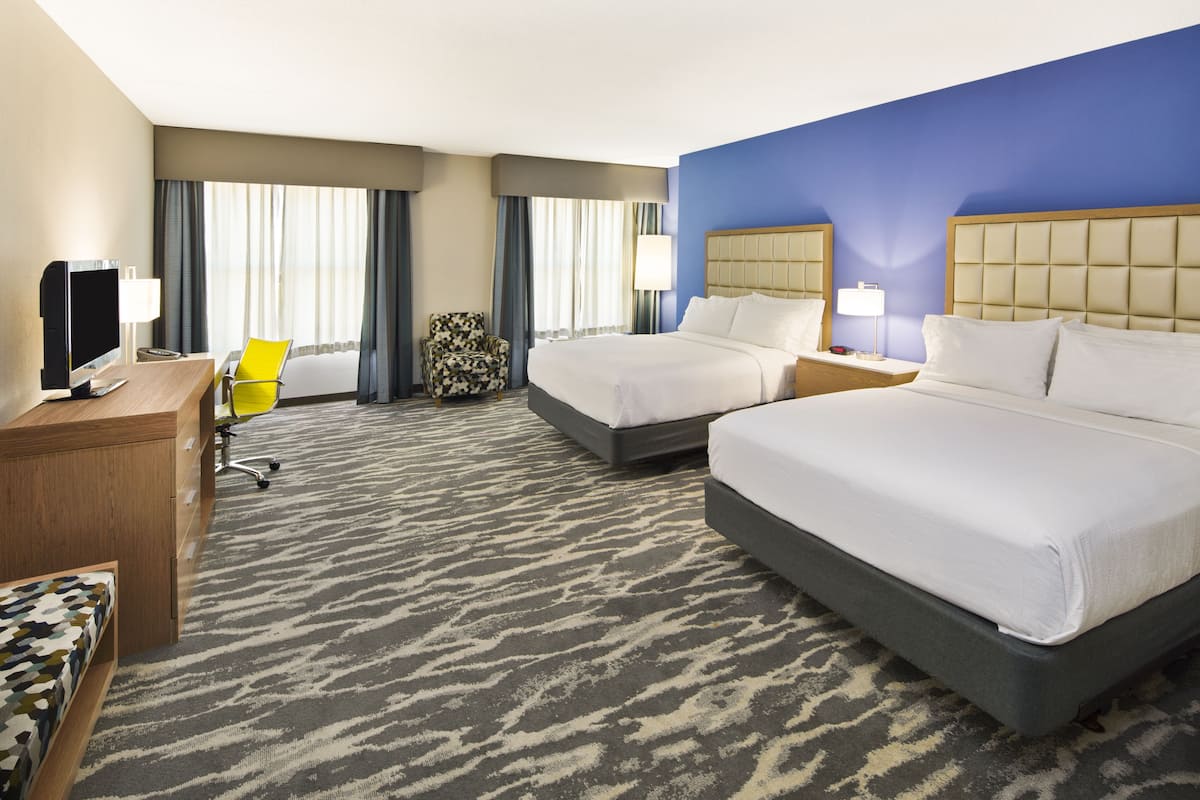 A hotel room with two beds, a desk with a computer, a chair, and a large window with curtains.