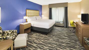A hotel room with a bed, bedside tables, a desk with a chair, a television, and a window with curtains.