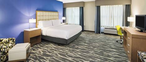 A hotel room with a bed, a desk, a chair, a TV, and a window with curtains.