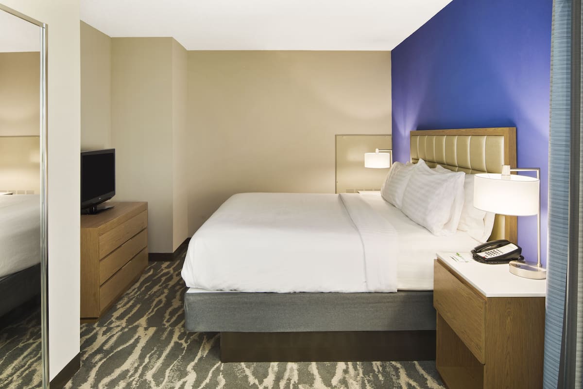 A hotel room with a bed, bedside tables, a TV, and a lamp.