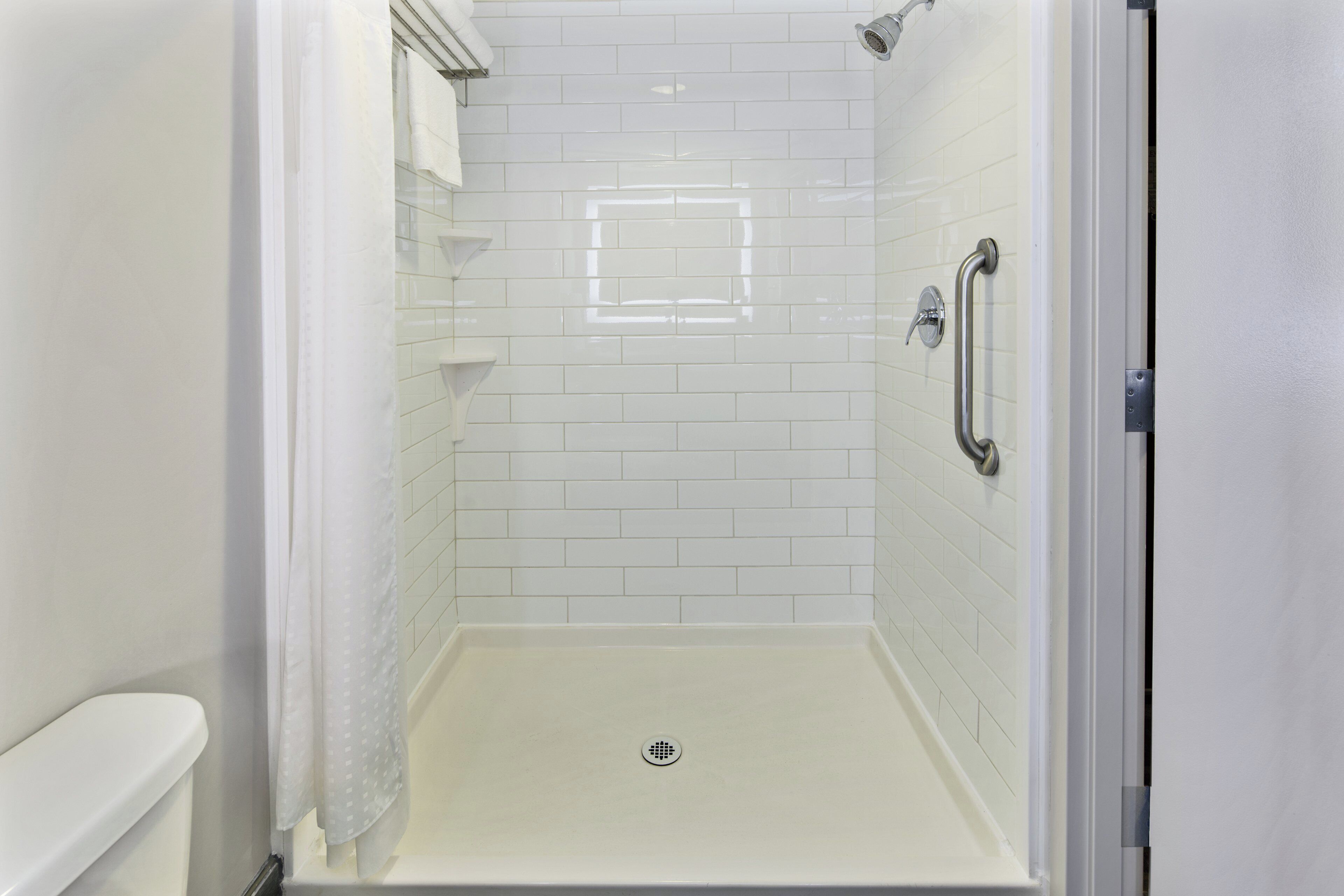 Une douche à l’italienne avec des murs et un sol recouverts de carreaux blancs.